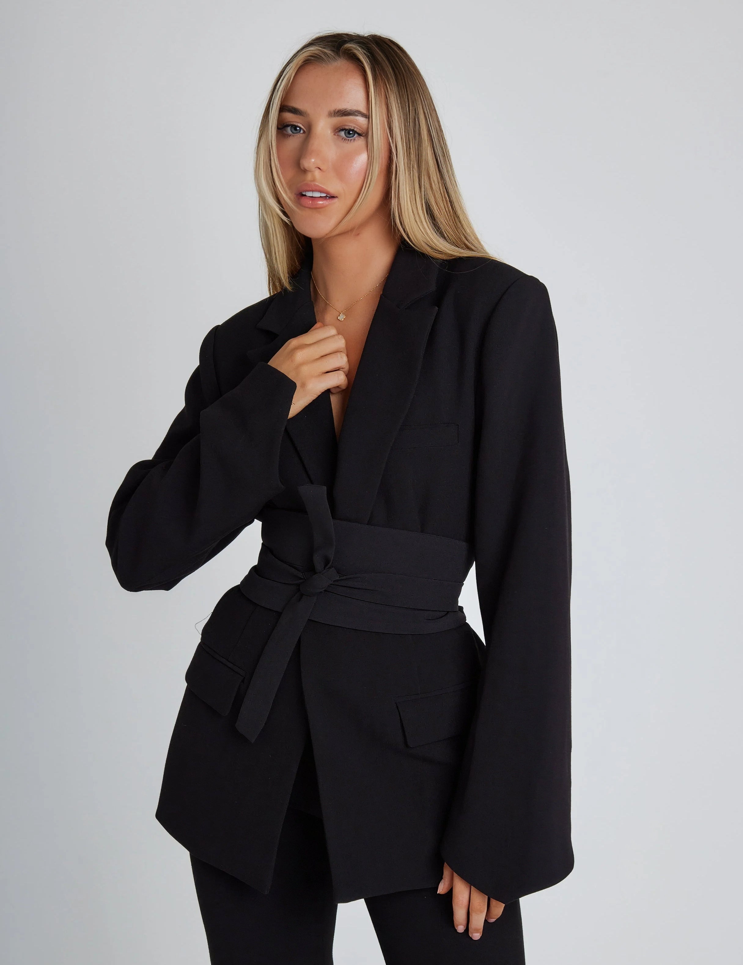 Black blazer with deep V neckline, long sleeves, waist tie belt, and flap pockets