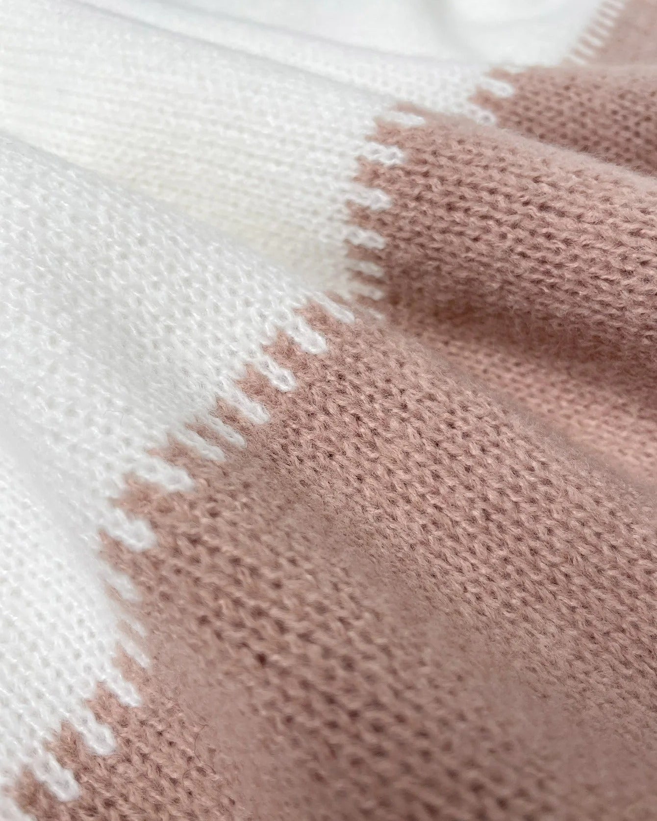 Knit close-up of pullover: cream and blush-pink panel with textured border