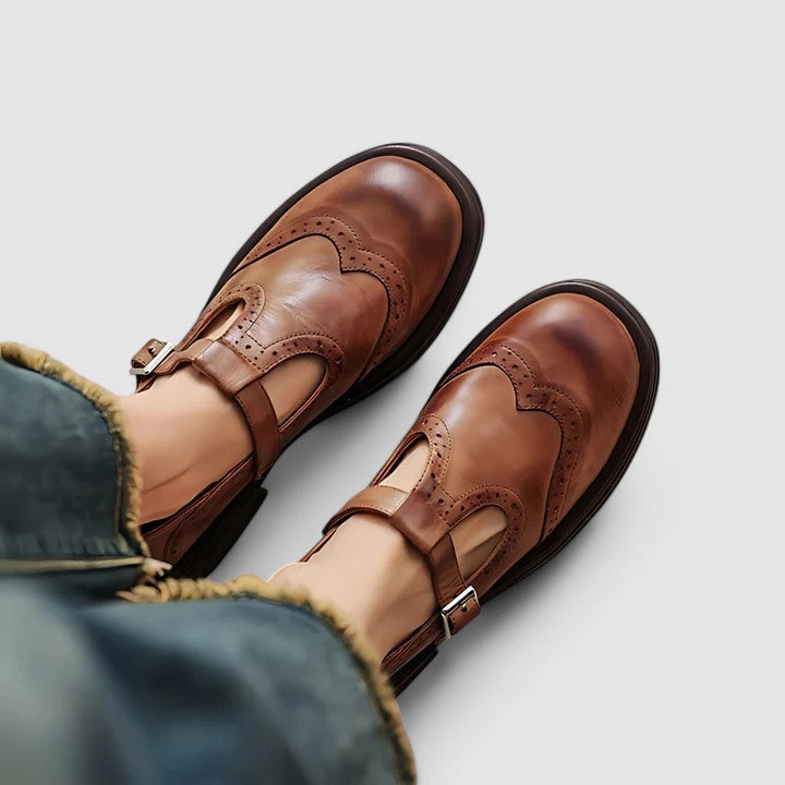 Brown leather Mary Jane flats with ankle strap and buckle, brogue-style detailing.