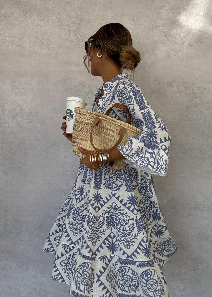 Blue-and-white patterned V-neck mini dress with long sleeves and ruffled, flared hem.