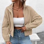 Cropped long-sleeve beige jacket worn open over a white top, with snap buttons and pockets.