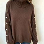 Oversized brown knit turtleneck pullover with buttoned cuffs and long sleeves