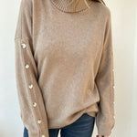 Oversized beige knit turtleneck pullover with buttoned cuffs, long sleeves