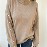 Oversized beige knit turtleneck pullover with buttoned cuffs, long sleeves