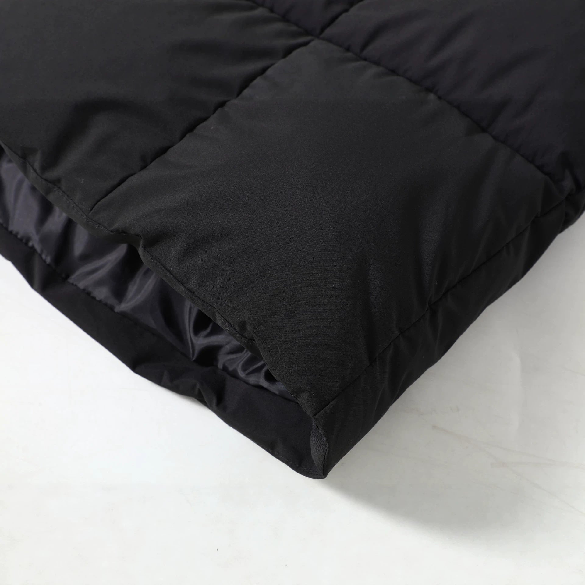 Black quilted parka fabric close-up with long hem and snap button placket