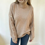Oversized beige knit turtleneck pullover with buttoned cuffs, long sleeves