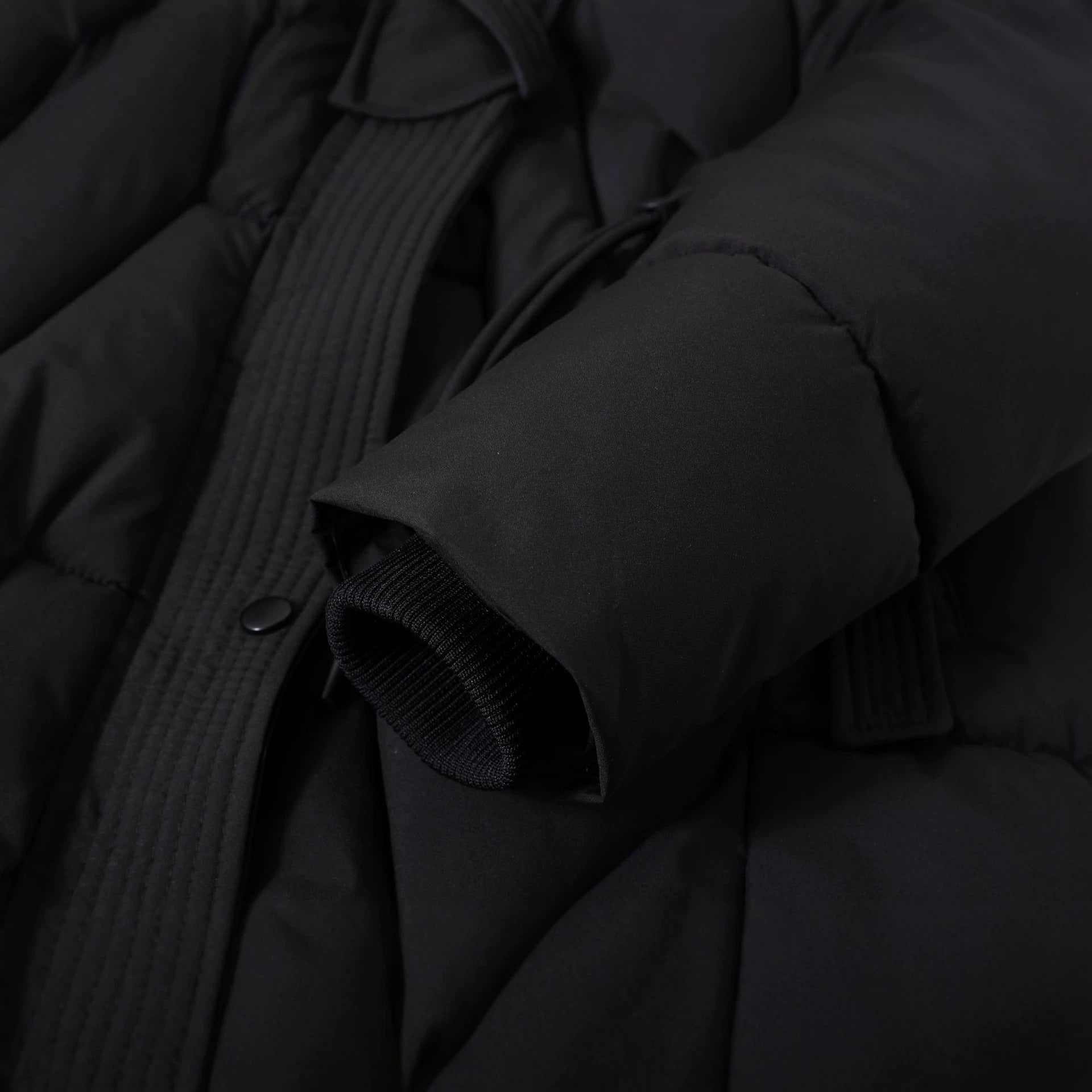 Black parka collar and sleeve close-up with ribbed inner cuff and button detail
