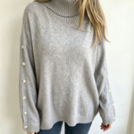 Oversized light gray knit turtleneck pullover with buttoned cuffs, long sleeves