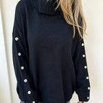 Oversized black knit turtleneck pullover with buttoned cuffs, long sleeves