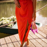 Orange midi dress with front slit and tie belt detail; purple heels visible