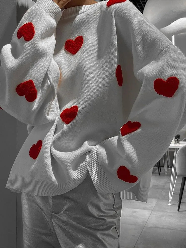 White knit pullover close-up with small red hearts and ribbed cuffs.