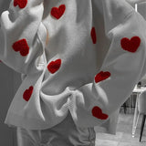 White knit pullover close-up with small red hearts and ribbed cuffs.