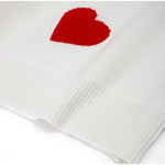 White knit fabric swatch with red heart patch and visible ribbed hem.