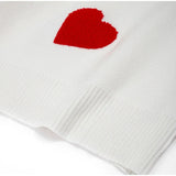 White knit fabric swatch with red heart patch and visible ribbed hem.