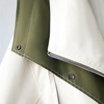 Close-up of jacket panel seam with snap buttons on olive-green and cream contrast