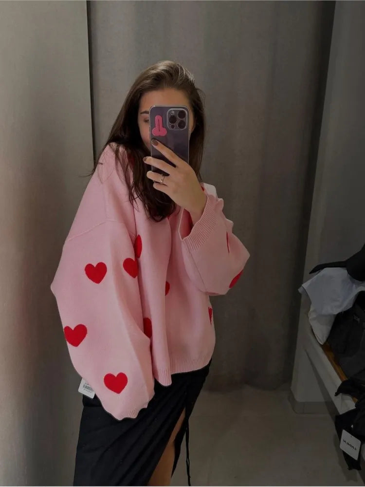 Light pink pullover sweater with red heart print, long sleeves and ribbed cuffs.