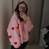 Light pink pullover sweater with red heart print, long sleeves and ribbed cuffs.