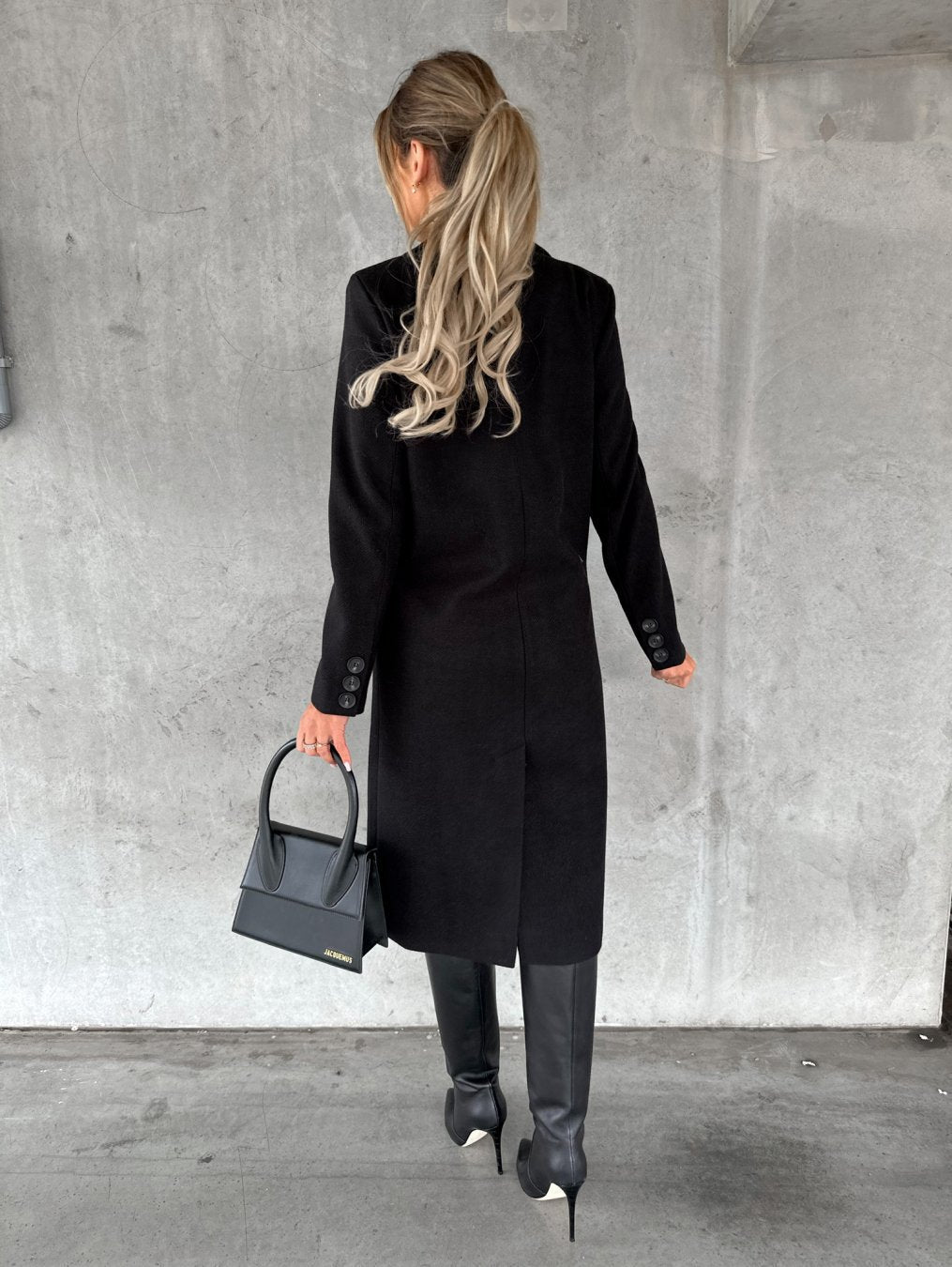 Black double-breasted overcoat from back view with long sleeves and buttoned cuffs