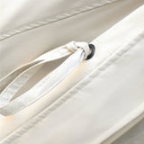Close-up of cream jacket drawstring with black grommet and stitched panel