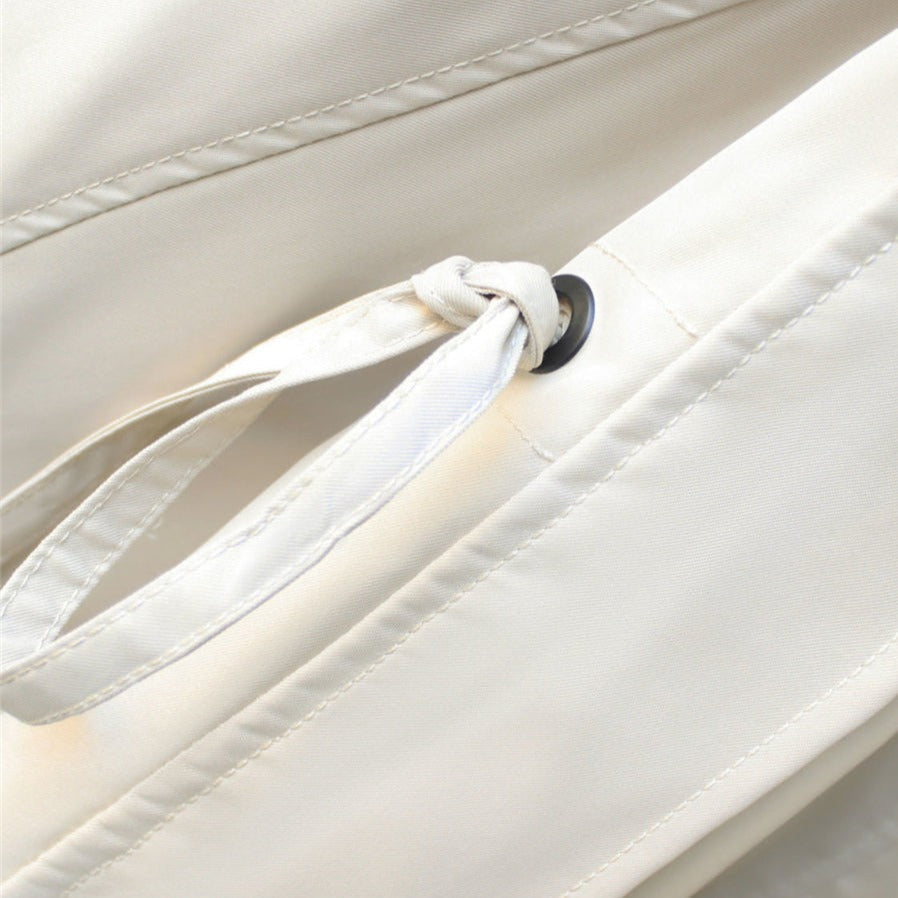 Close-up of cream jacket drawstring with black grommet and stitched panel