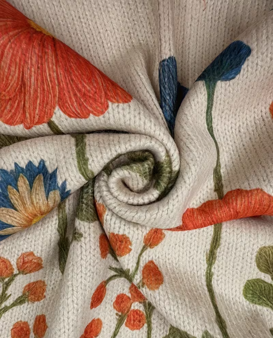 Cream knit cardigan fabric close-up with zipper seam and orange-blue floral pattern