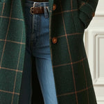 Dark green plaid coat with two front buttons and long hem, worn over blue jeans