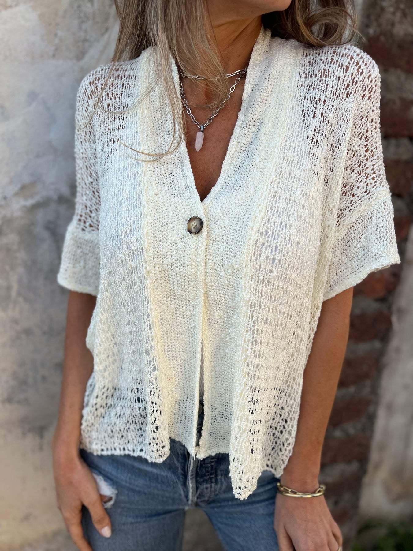 Light beige textured blouse with V-neck, short sleeves, and gold button closure